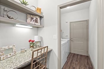 A hallway with wood/vinyl flooring, a built-in desk with wall shelves, a laundry room with washer & dryer included, and a door to the attached garage.